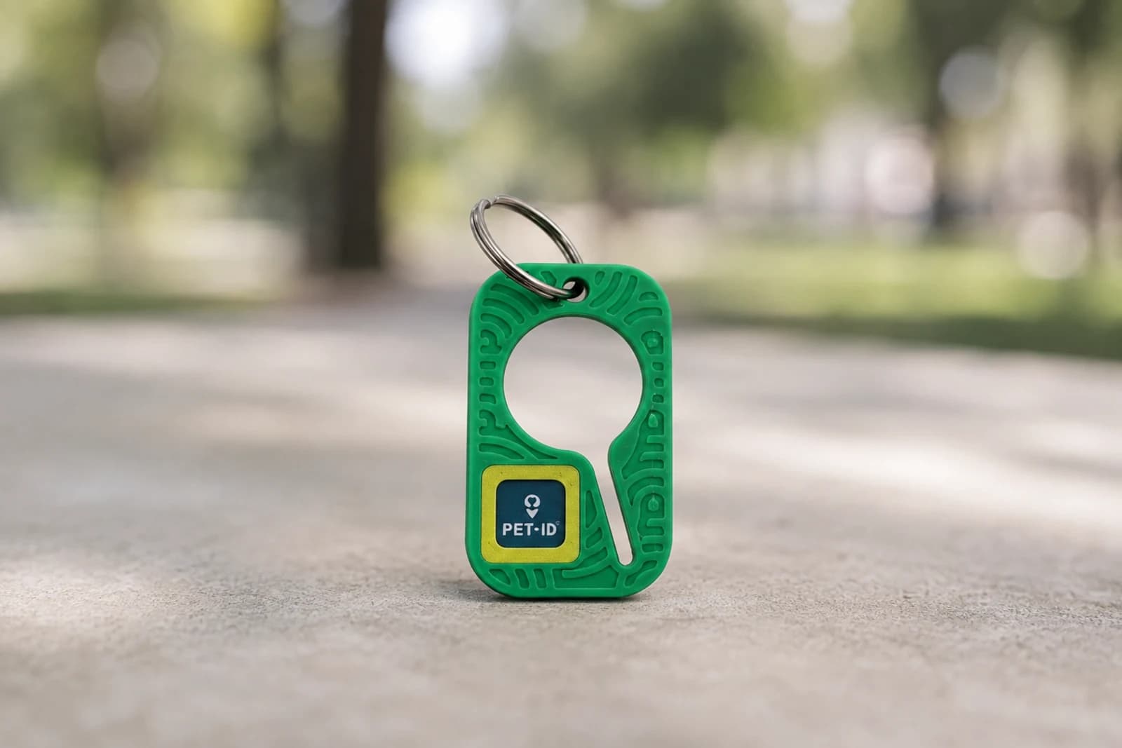 Portabolsas verde para mascotas con la placa de PET-ID al frente, de pie sobre el piso de un parque.